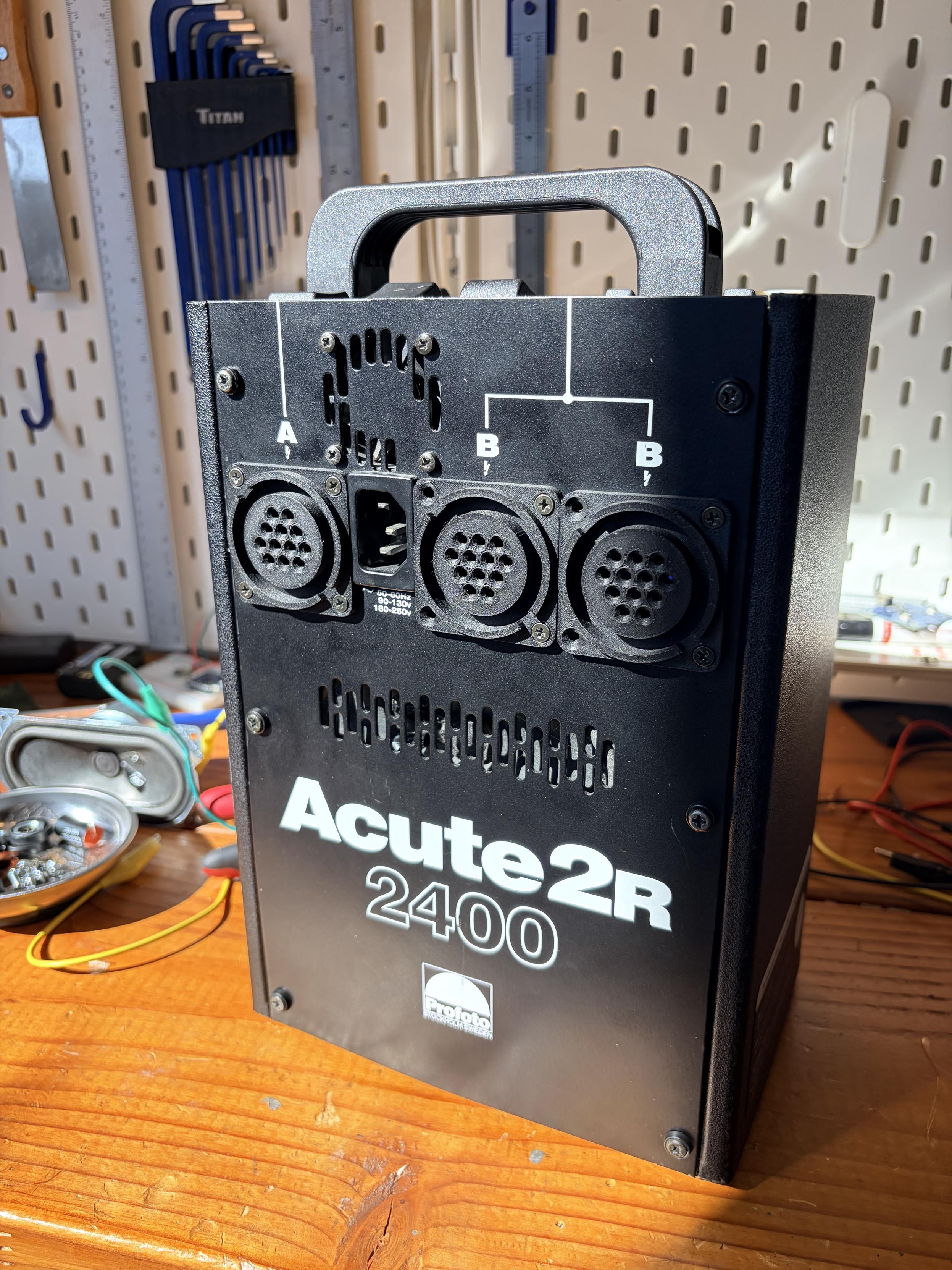 A normal looking Profoto Acute pack, which is just a black cube with a handle. On the front are three 3D printed dummy connectors where the strobe heads would have been connected